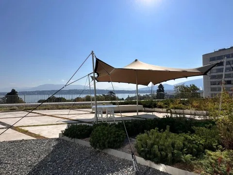 Shade sails on a terrace of the Palais des Nations can be seen, with Lake Geneva in the background.