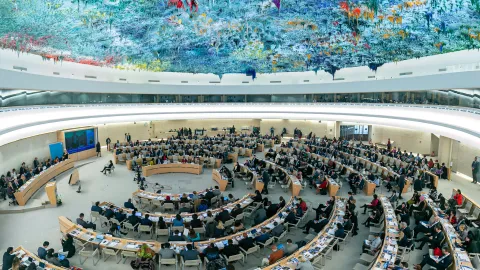 A picture of the Palais des Nations conference room XX is seen.